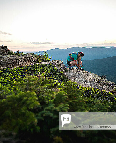 Trail runner man tying shoe with mountains behind him at sunrise