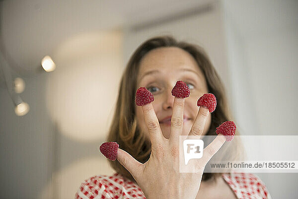 Pregnant woman holding raspberry on her fingers in the kitchen  Munich  Bavaria  Germany
