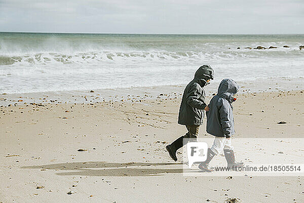 Two boys walking along beach with crashing waves