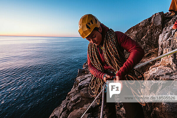 Woman rock climber getting ready to rappel on seaside cliff