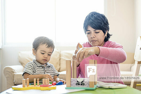 Latin mother and little son playing together with wooden logic toys.