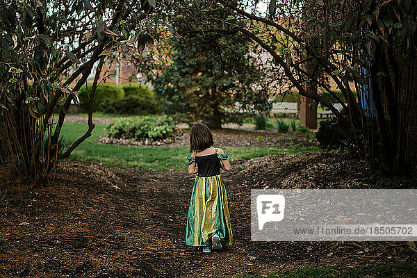 A little girl in a princess costume walks alone on a wooded path