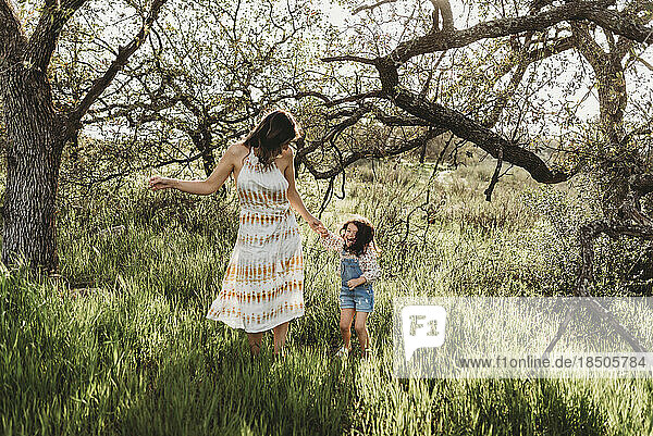 Mother and daughter holding hands and dancing in backlit meadow