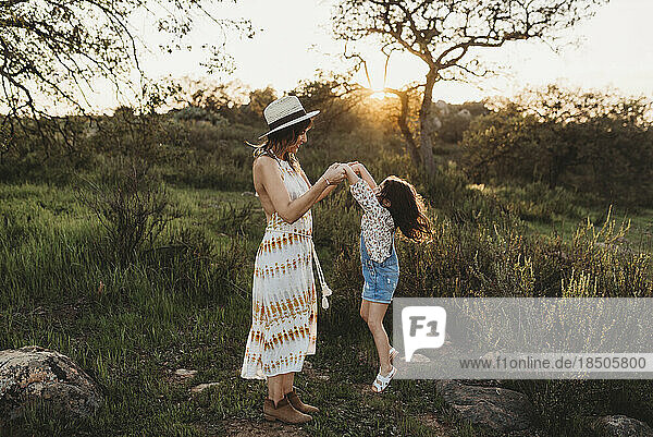 Full length view of young mother and daughter jumping in sunny meadow