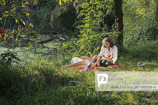 Couple having picnic and eating watermelon at riverbank  Bavaria  Germany