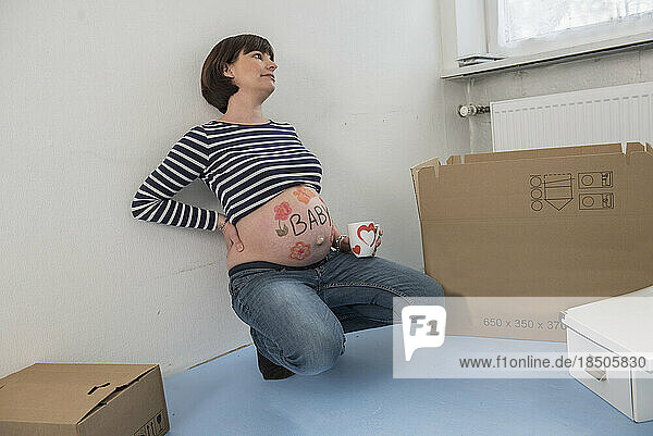 Pregnant woman holding mug and standing at window