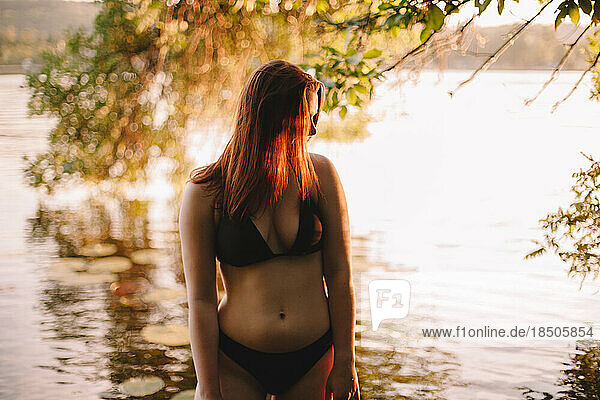 Woman in a bikini standing in lake under tree