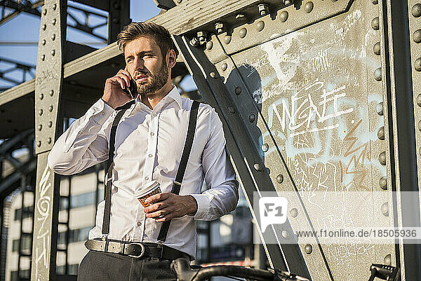 Businessman talking on mobile phone and drinking coffee  Munich  Bavaria  Germany