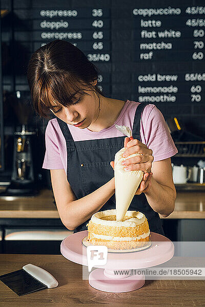 Woman in a dark apron decorate cake  squeezes out vanilla cream on cake in kitchen cafe