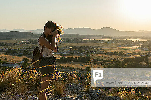 Young woman is taking a photo with her camera on top of a mountain