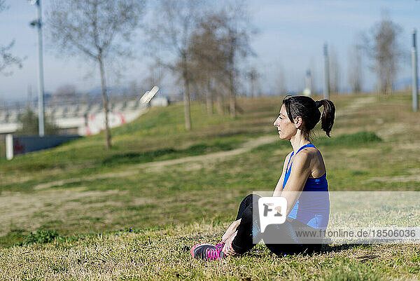 Female athlete meditating while sitting on grass at park in sunny day