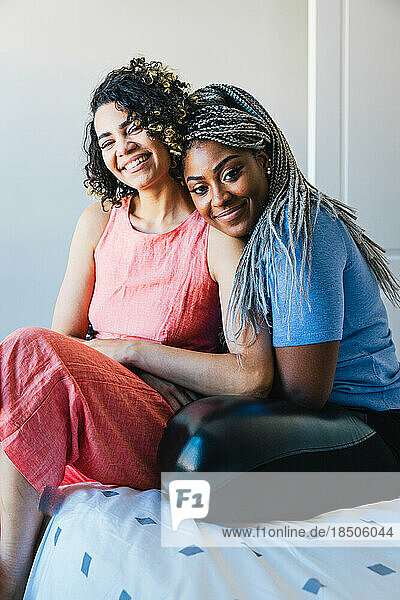 Portrait of happy lesbians sitting on bed at home