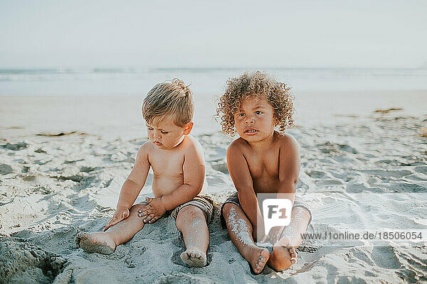 Mixed race toddler boy twins sitting and playing in sad