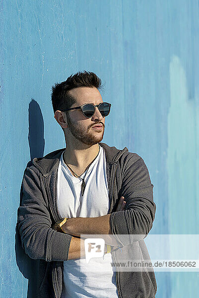Portrait of young bearded man with sunglasses leaning against wall