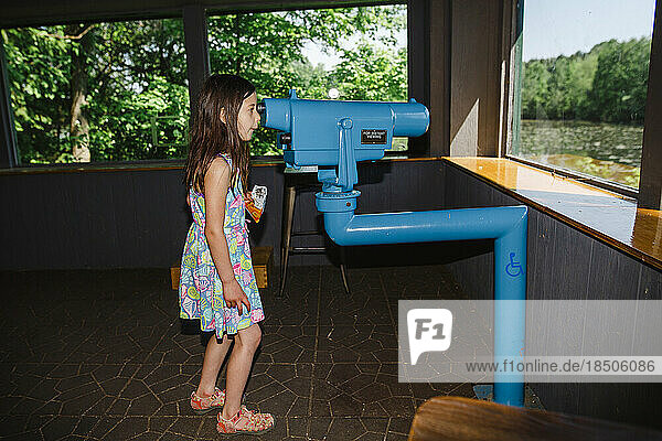 A little girl looks out through large binoculars at birds on pond