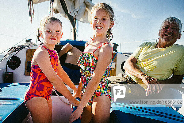 Young girls laugh and smile with Grandpa on sailboat in swimsuits