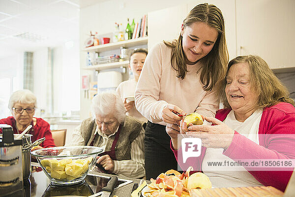 Senior woman with girl cutting apple at rest home