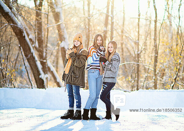 Three tween girls drinking coffee in the snow on winter day.
