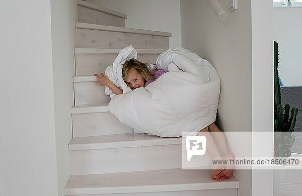young blonde girl playing wrapped up in a duvet cover on the stairs