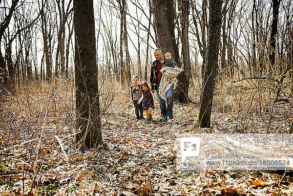 Father walks in woods with children holding baby and daughters hand