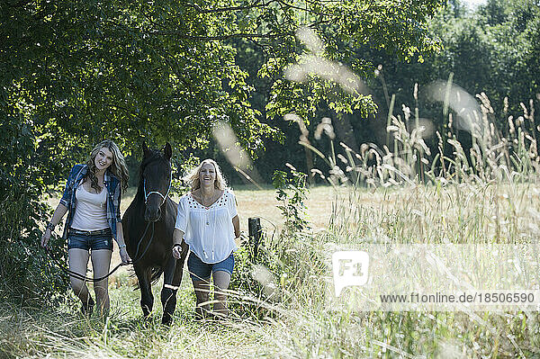 Two women walking with a horse on meadow and smiling  Bavaria  Germany