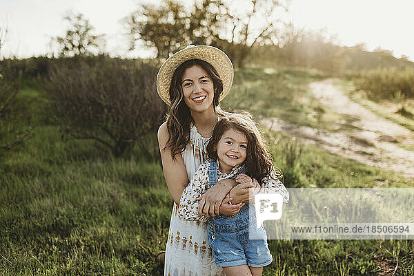 Portrait of happy young mother and daughter smiling in backlit meadow