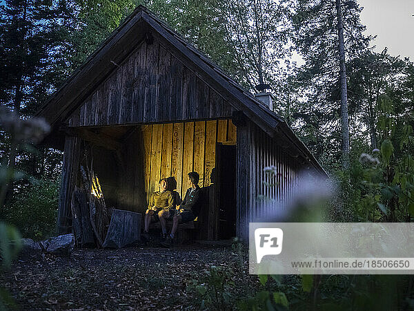 Two male hikers relaxing in front of small hut in Black Forest at night  Baden-Württemerg  Germany