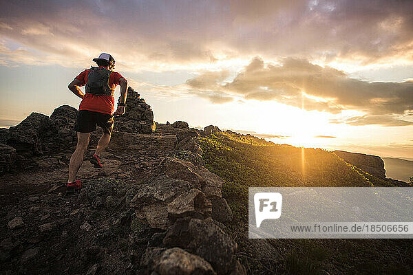 Trail running man running at sunrise with cairn from low angle
