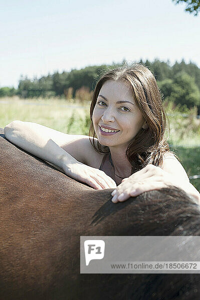 Portrait of a mature woman leaning on her brown horse's back and smiling  Bavaria  Germany