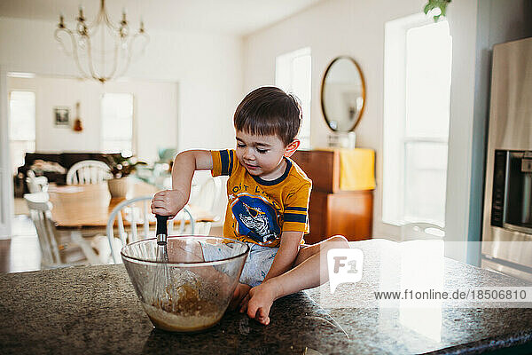 Young boy sitting on counter mixing batter with wisk