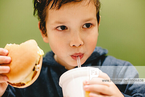 Boy eating and drinking against green background