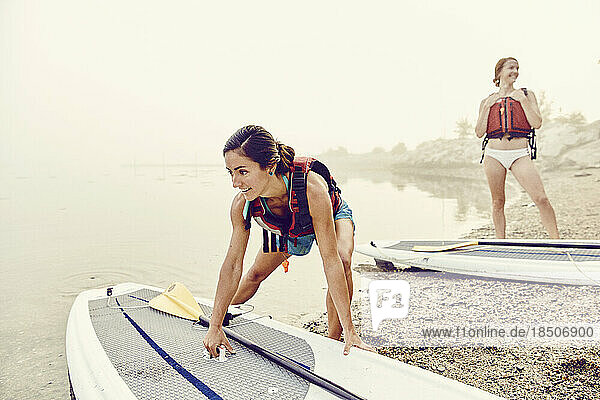 Young women launch their paddle boards into water on a foggy morning
