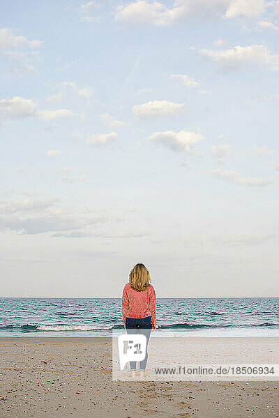 Young woman walks along the coast watching the sea