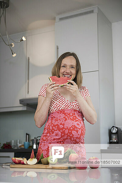 Portrait of a pregnant woman eating watermelon in the kitchen  Munich  Bavaria  Germany