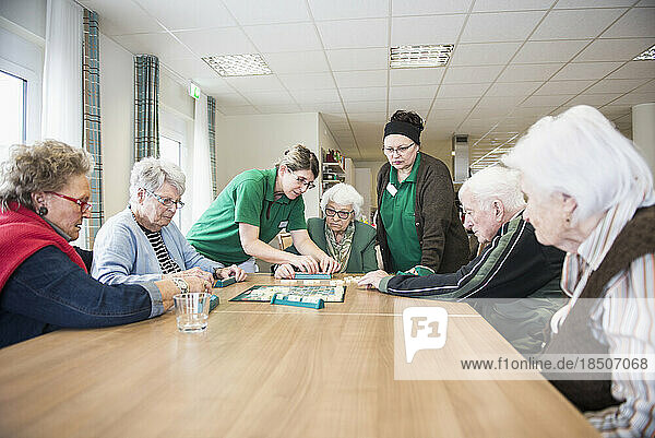 Senior inhabitants playing board game with nurse in rest home