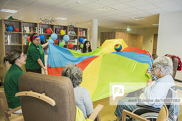 Nursing staff with girls and senior women doing sports exercise using parachute and ball in rest home