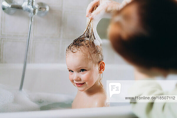 Woman bathes a little happy girl  Shampooing her hair