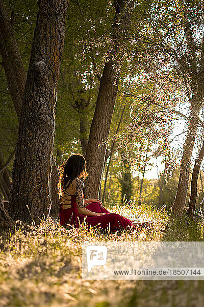 Young woman in a red dress lying in a forest at sunset