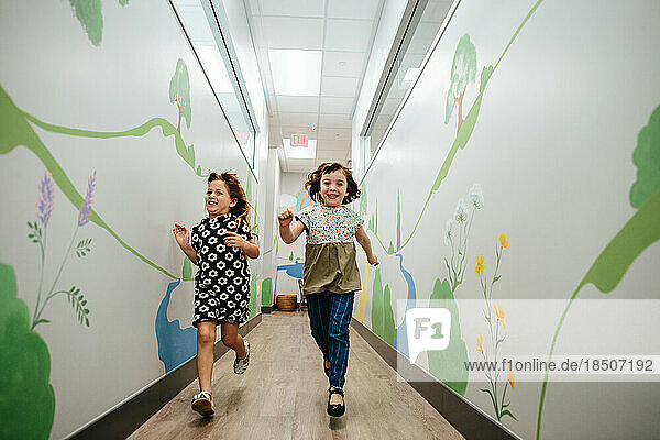 Two girls smile and run down a hallway in a school building