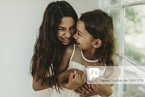 Sisters hugging in natural light studio while looking at each other