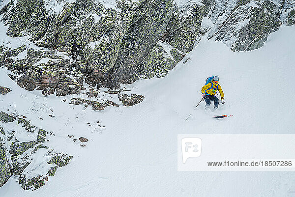 Backcountry skier skiing snow with tall rock walls on each side