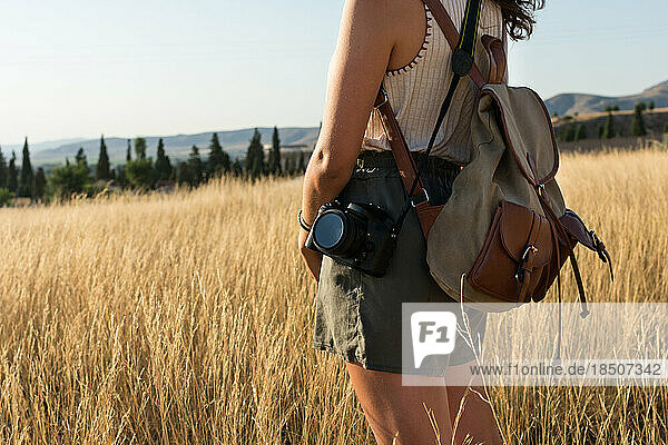 Young woman with a backpack and a camera in a meadow at sunset.