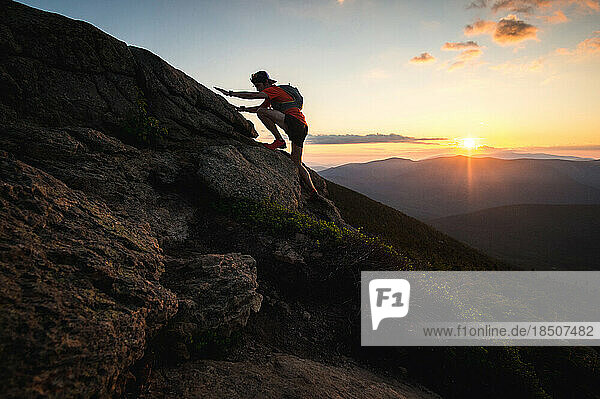 Silhouetted trail runner man scrambling in rocks at sunrise