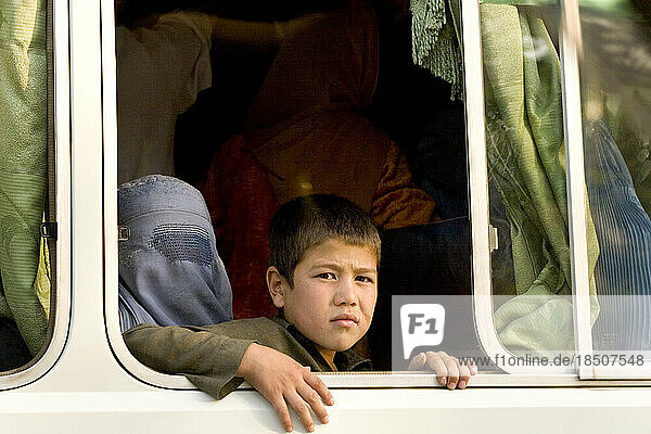 Woman in burka and a boy look out from the window of a crowded Kabul city bus.