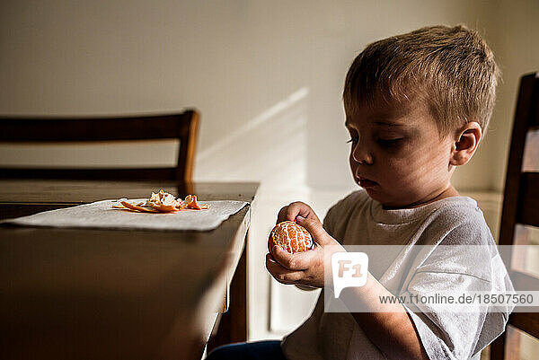 Toddler peeling clementine at kitchen table
