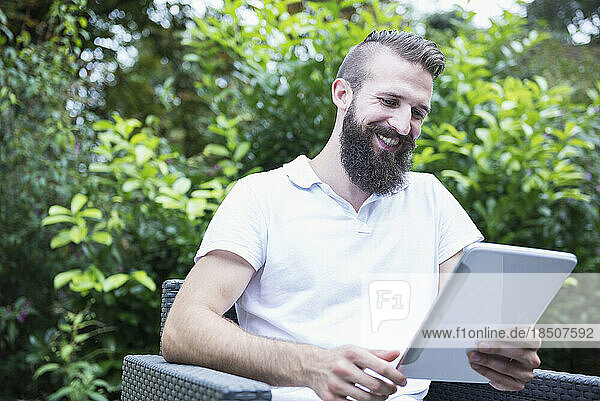 Happy young man sitting on a chair and using digital tablet in garden  Bavaria  Germany