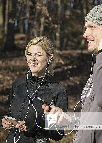 Man and woman in sportswear listening music on smart phone in forest