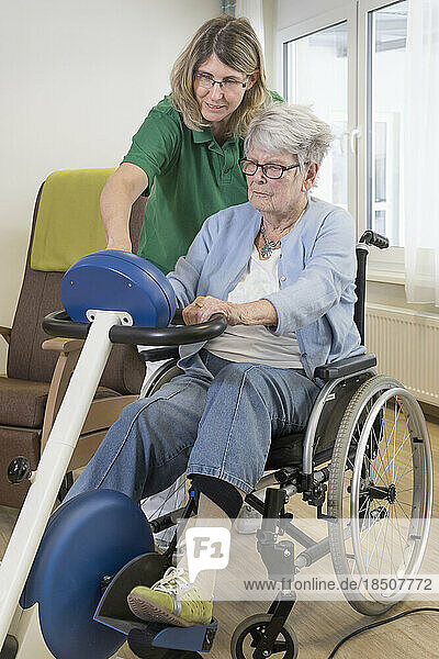 Nurse with senior woman on wheelchair exercising on exercise bike in rest home