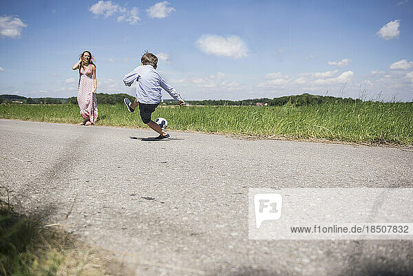 Small boy playing football with his mother on road in the countryside  Bavaria  Germany