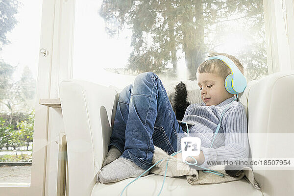 Boy listening music using digital tablet and headphones on armchair